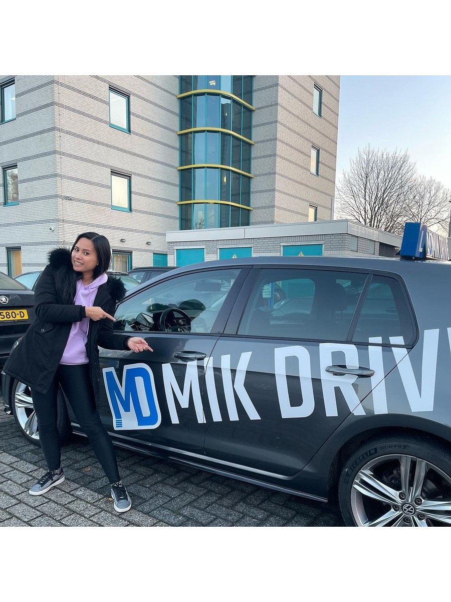 Geslaagde leerling met het MikDrive-bord bij de lesauto